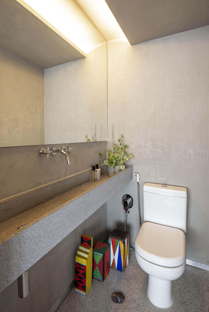 In this modern bathroom, a long concrete trough sink lines the wall, while hidden lighting in the ceiling creates a warm glow. #TroughSink #BathroomDesign #BathroomIdeas