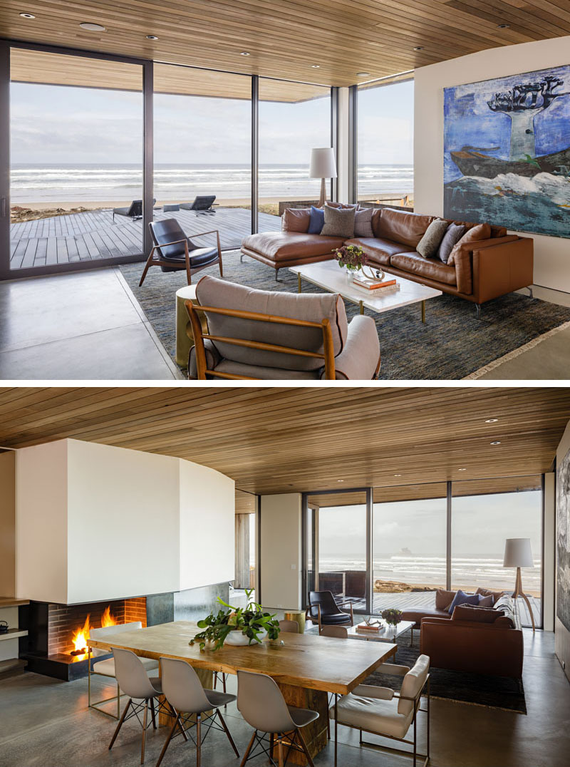 In this modern beachfront living room, floor-to-ceiling windows allow for ample natural light, while a door provides access to a deck, and on a cool night, a fireplace provides warmth. #LivingRoom #DiningRoom #Fireplace #Windows #Deck #WoodCeiling