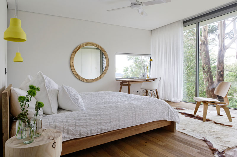 In this modern bedroom, a floor-to-ceiling window frames the trees, while a small work area takes advantage of a window to keep the desktop bright. #ModernBedroom #BedroomDesign