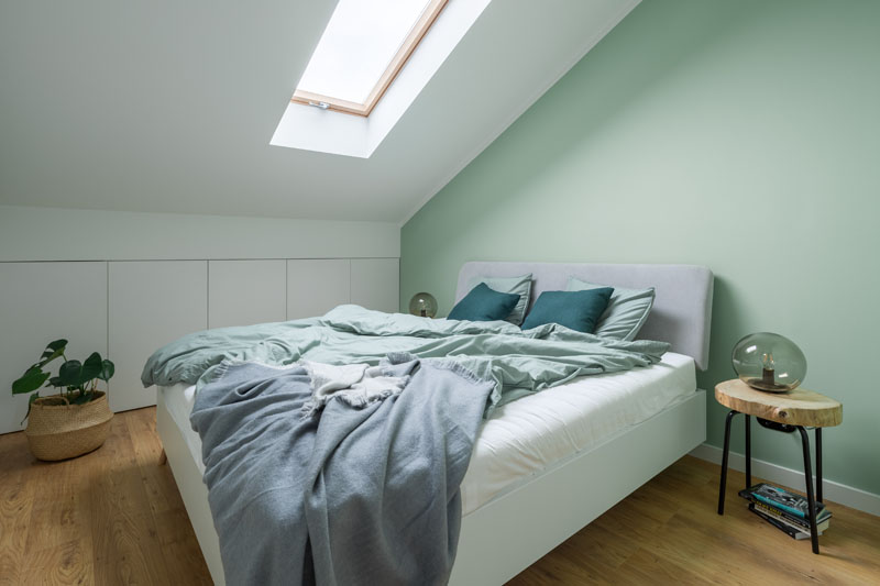 In this modern bedroom, a soft mint green accent wall provides a backdrop for the bed, while a skylight adds natural light to the room, and storage cabinets have been built into the wall. #ModernBedroom #BedroomIdeas #MintGreen