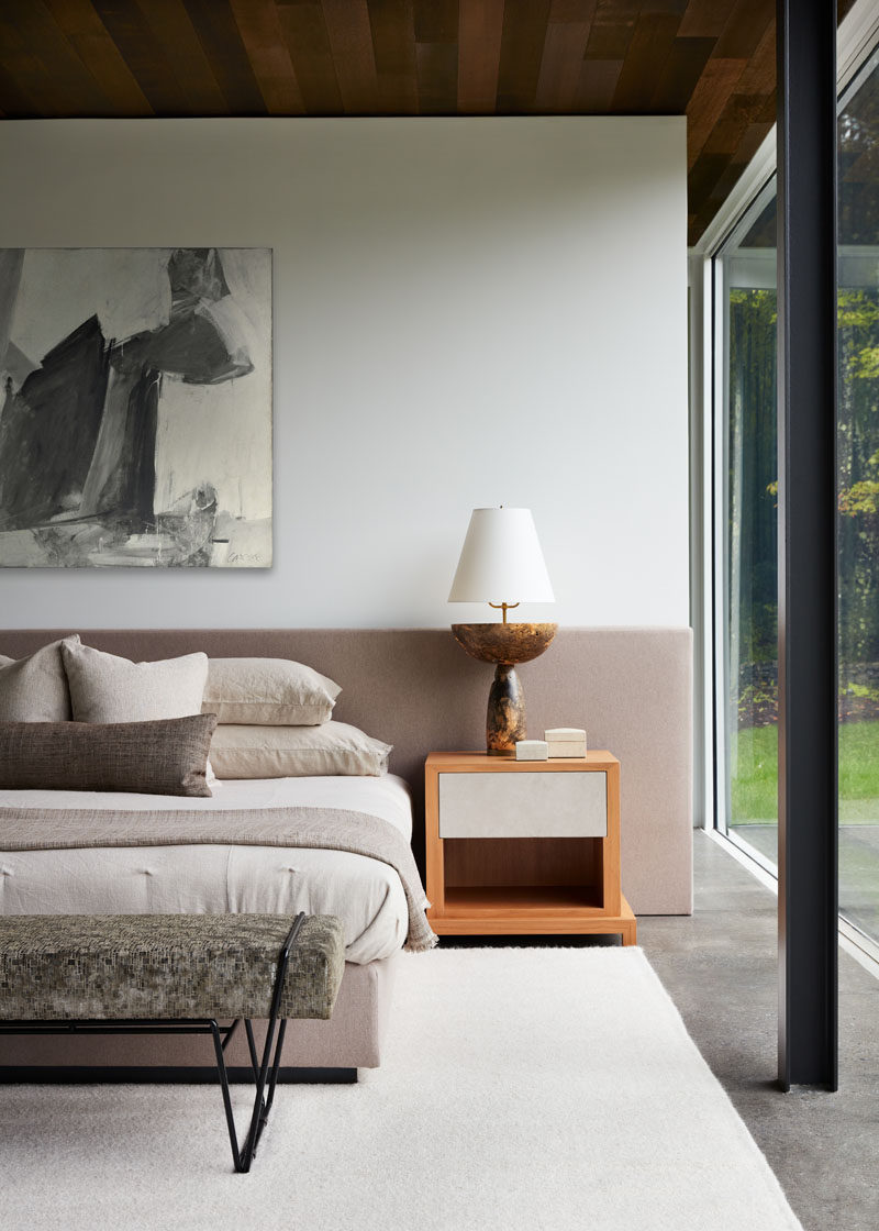 In this modern bedroom, the beside table lamps are the perfect height to complement the horizontal headboard, which provides a soft pop of color to the room. #ModernBedroom #BedroomDesign #GlassWalls