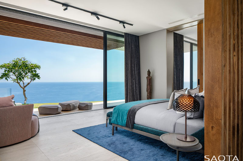 Floor-to-ceiling sliding doors connect this modern bedroom with a small patio, while inside, the blue accents complement the water views. #ModernBedroom #BedroomDesign