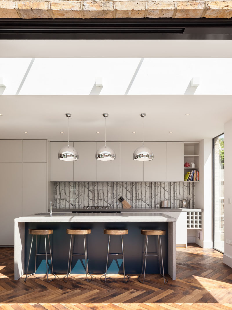 In this modern kitchen, clean-lined white cabinets contrast with the pop of blue used on the island. #WhiteKitchen #KitchenDesign #ModernKitchen