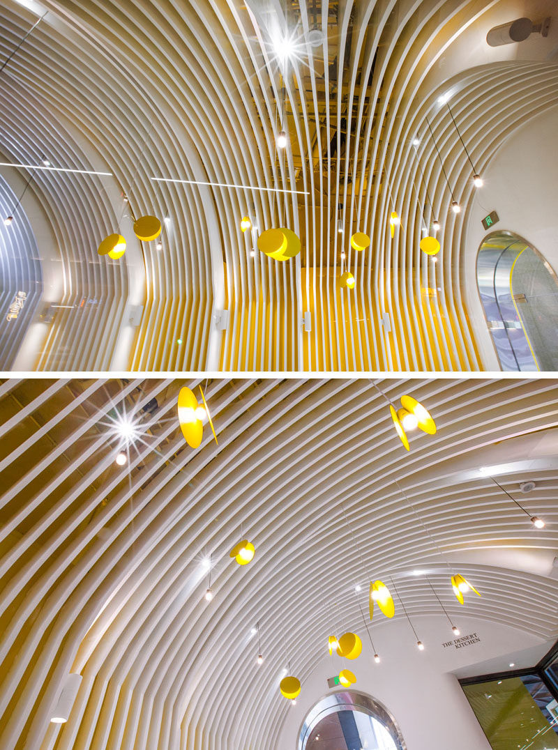 The fin covered vaults in this modern cafe assist in concealing the air conditioning vent, while the yellow painted walls behind the fins aid in creating a soft color palette that connects to the bold yellow facade and bar counter. #InteriorDesign #RetailDesign #CafeDesign