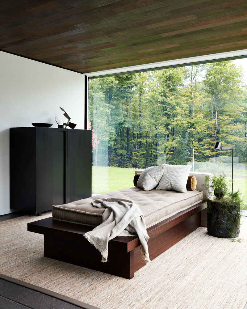 A daybed is centrally positioned in this room with a wood ceiling and glass walls, providing a place for the home owner to relax and enjoy the tree views. #Daybed #InteriorDesign #GlassWalls