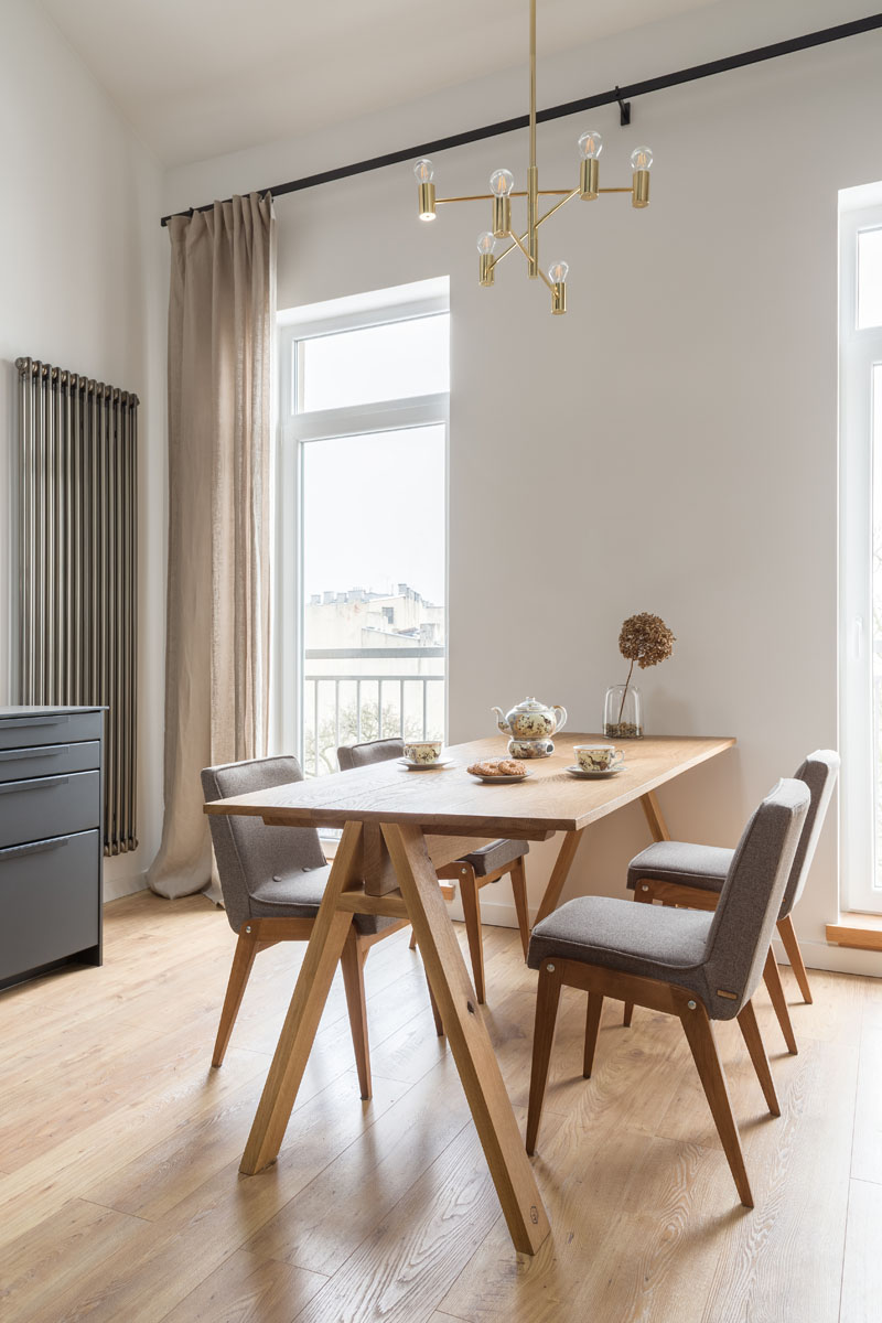 A solid wood oak dinner table is anchored in this apartment by a minimalist chandelier, that draws the eye upwards to showcase the height of the ceiling. #DiningRoom #ModernApartment #InteriorDesign