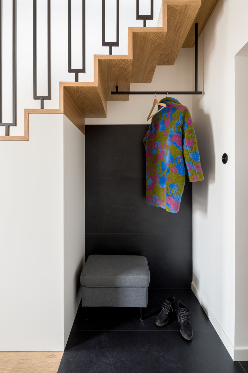 Stepping inside this modern apartment, there's a small entryway with large-scale black tiles that wrap from the floor onto the wall of an alcove underneath the stairs. This alcove provides a place to hang coats and take off shoes, and adjacent to the alcove and underneath the stairs are closets for extra storage. #ModernApartment #Entryway #InteriorDesign