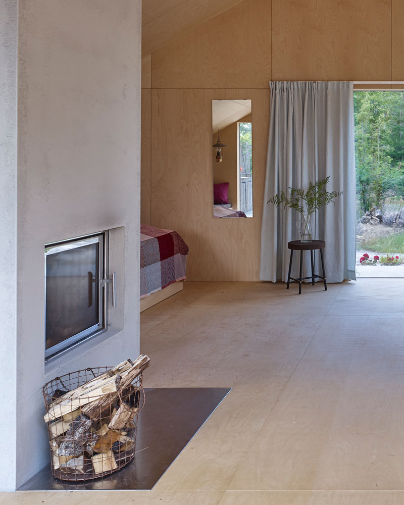 A concrete fireplace surround with a steel hearth separates the lounge area from the sleeping area. #Fireplace #PlywoodInterior #ModernInterior