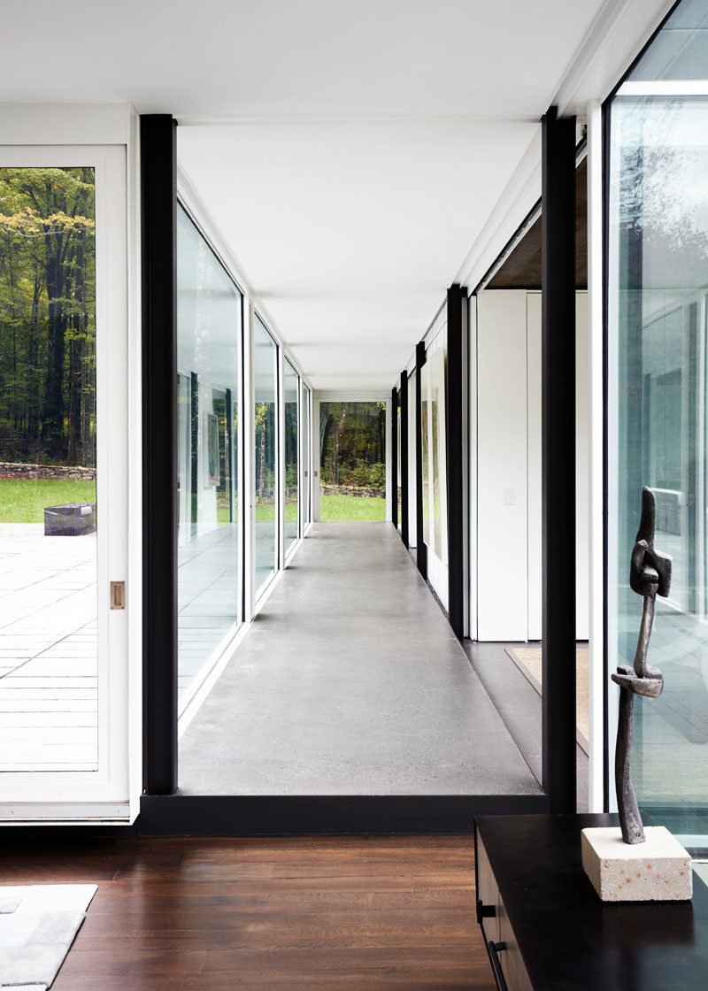 The floor-to-ceiling glass walls throughout this modern house fill the interior with an abundance of natural light. #ModernHouse #GlassWalls #Hallway