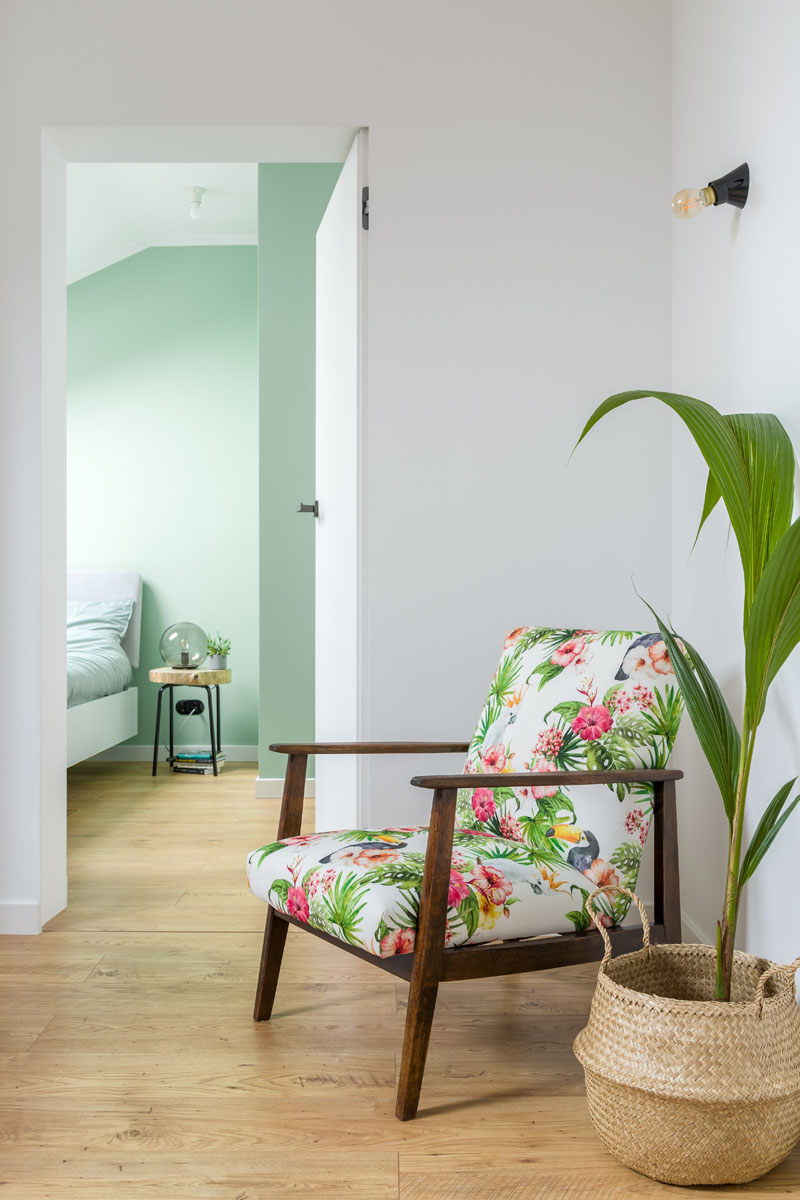 A white door that blends into the wall by the floral armchair at the top of the stairs, provides access to the bedroom in this modern apartment. #InteriorDesign #MintGreen #Interiors #Apartment