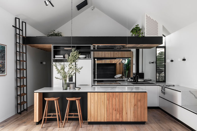 In this modern kitchen, a large island with black accents complements the black edge of the loft, while a mirrored backsplash reflects the backyard. #ModernKitchen #KitchenDesign #BlackAccents