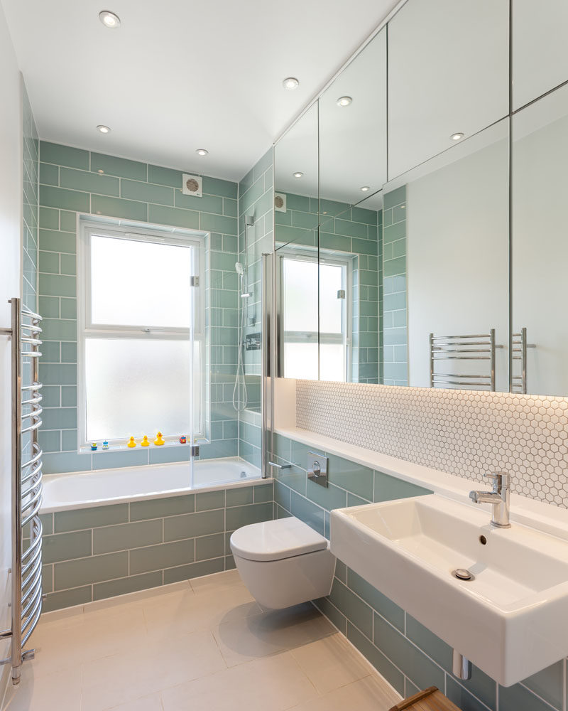 In this modern bathroom, light green subway tiles have been paired with white penny tiles and a large group of mirrors. #GreenTiles #ModernBathroom #BathroomDesign