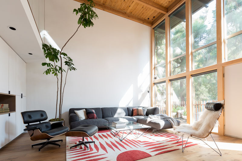 Large double-height, wood framed windows flood the updated interior with natural light. The bright interior strongly contrasts the dark exterior of the house. #LivingRoom #MidCenturyModern #Windows