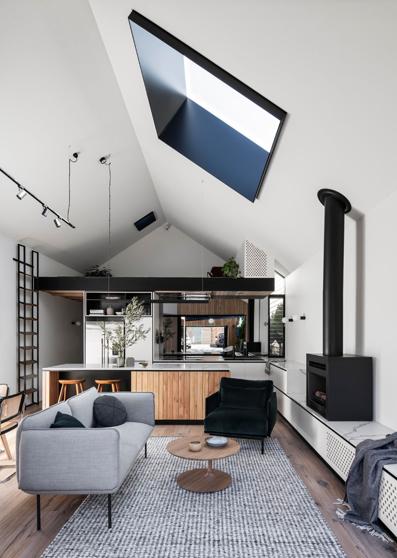 In this modern interior, the vaulted ceiling creates a tall and open space for the new living room, dining room, kitchen, and loft area. In the living room, the couch is focused on the black fireplace, that sits on a custom built low shelf. #ModernInterior #LivingRoom #Skylight #VaultedCeiling #BlackFireplace