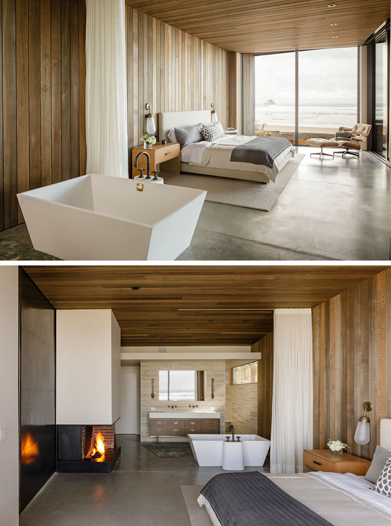 In this modern master bedroom, wood walls has been installed to match the wood ceiling, while the ensuite bathroom has been left open, allowing for water views from the bathtub. #MasterBedroom #WoodWalls #WoodCeiling #OpenBathroom #Fireplace