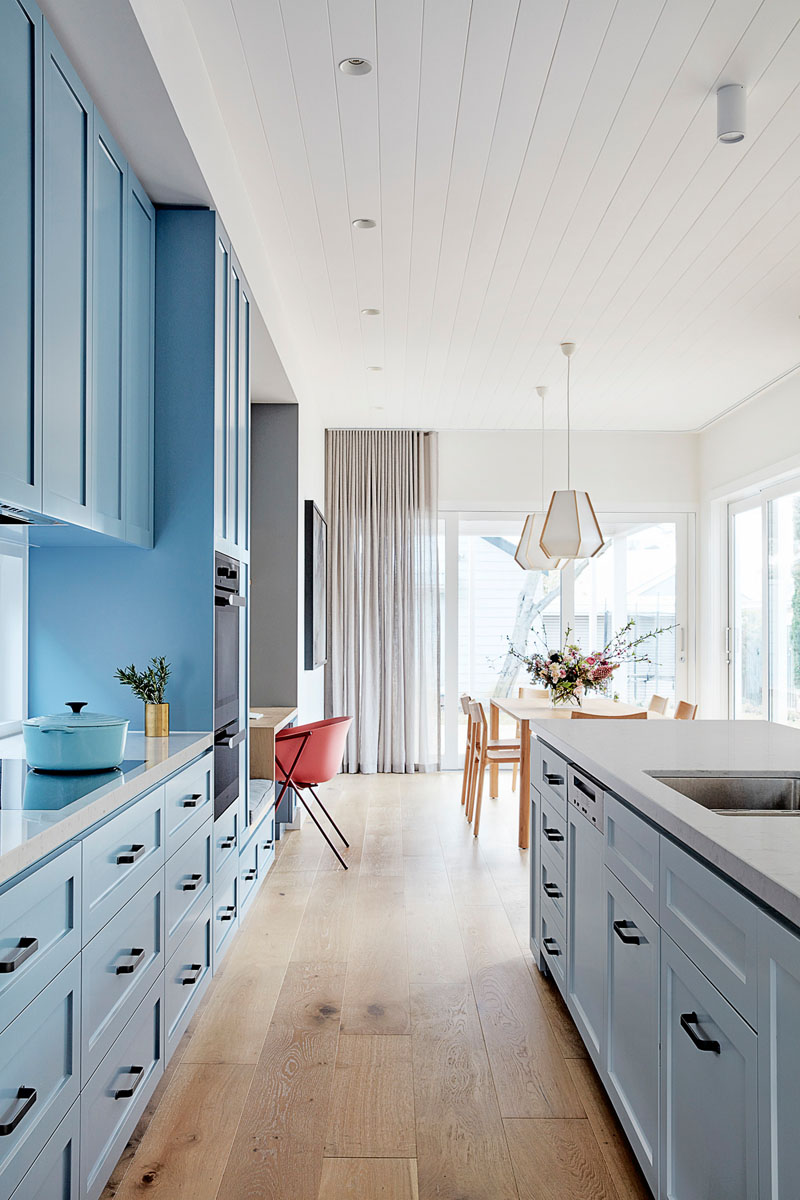 In this modern kitchen, matte light blue cabinets line the wall and transform into a small built-in home office with a bench, while a large white kitchen island provides additional seating. #LightBlueKitchen #ColorfulKitchen #KitchenIdeas #HomeOffice