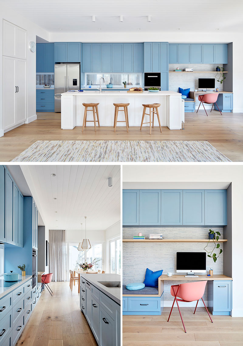 In this modern kitchen, matte light blue cabinets line the wall and transform into a small built-in home office with a bench and desk, while a large white kitchen island provides additional seating. #LightBlueKitchen #ColorfulKitchen #KitchenIdeas #HomeOffice