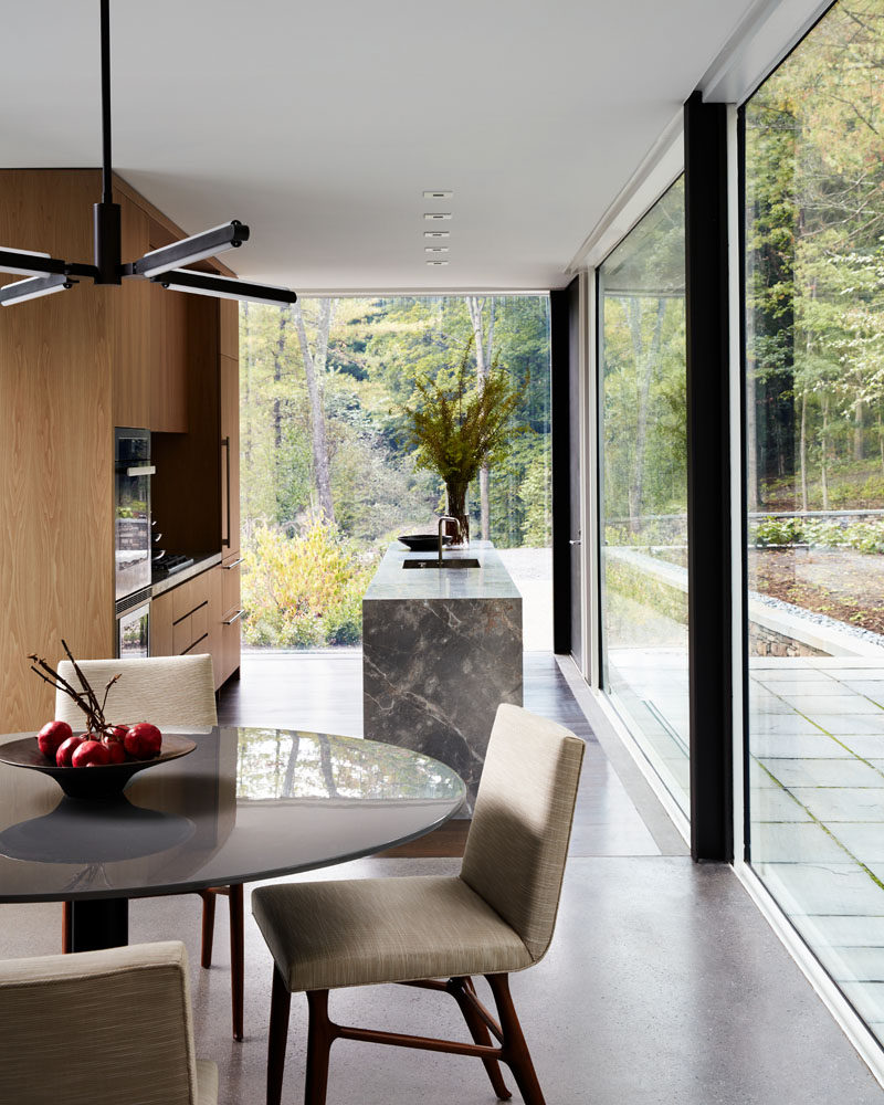 In this modern kitchen, wood cabinets have been combined with a grey countertop for a contemporary look, while floor-to-ceiling glass walls fill the room with natural light. #Kitchen #Windows #GlassWalls