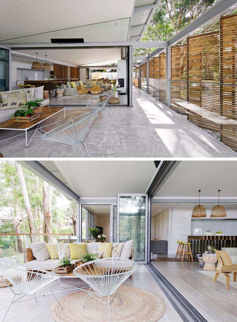 Folding glass doors open the living room in this modern house to a secondary outdoor living room, that's furnished with another couch and has views of the trees. #OutdoorLivingRoom #ModernInterior #GlassDoors