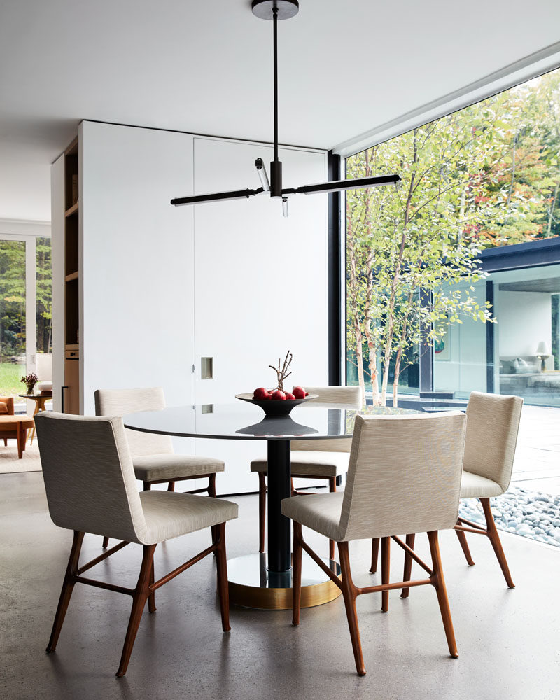 In this modern dining room, a round dining table with a glossy top reflects the light, while a four-armed pendant light hangs above. #ModernDiningRoom #InteriorDesign