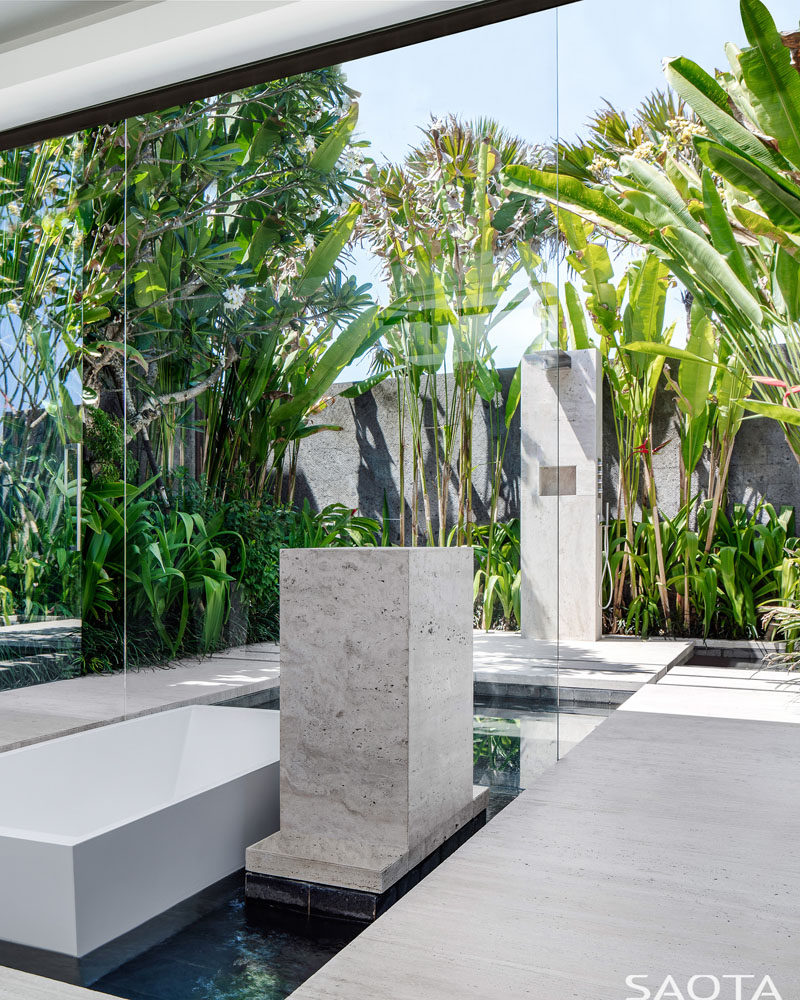 In this modern master ensuite bathrooms, a sunken bathtub is surrounded by a water feature that flows to the outdoors, where an outdoor shower is surrounded by lush landscaping. #SunkenBathtub #OutdoorShower #ModernBathroom