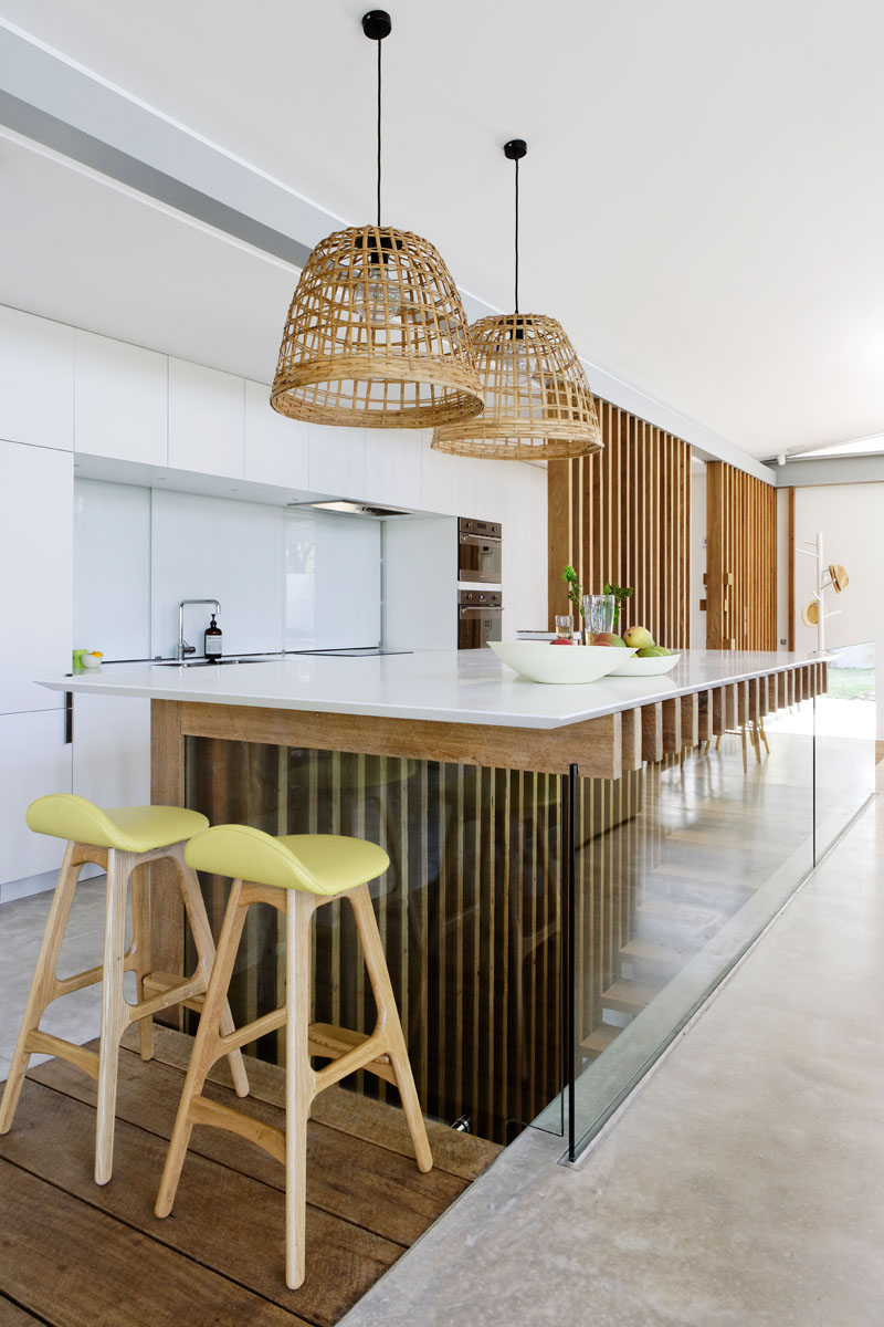 In this modern kitchen, minimalist white cabinets line the wall, while wood fins and glass support the kitchen island countertop. #ModernKitchen #KitchenDesign #WhiteKitchen