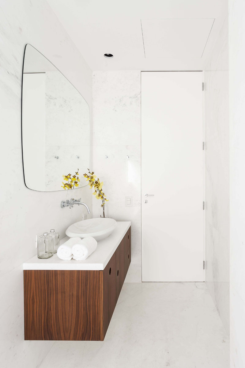 In this modern bathroom, a floating wood vanity and some flowers add a natural touch to the mostly white room. #BathroomIdeas #ModernBathroom #WoodVanity