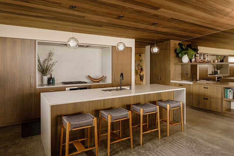 Wood ceilings and concrete flooring with radiant heating are featured throughout this modern beachfront house, while in the kitchen, a rift-sawn Oregon white oak has been used for the cabinets with a light colored countertop providing contrast. #WoodKitchen #WoodCeiling #ConcreteFloors