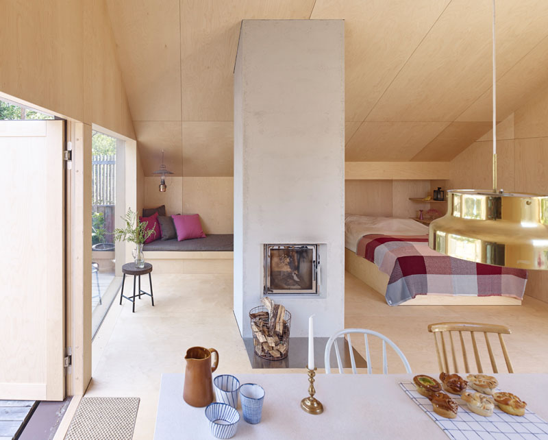 Windows filter the light through to the bright interior of this modern house that features birch plywood walls, ceiling, and floor. #PlywoodWalls #PlywoodInterior #Windows #LivingRoom #Fireplace #Bedroom