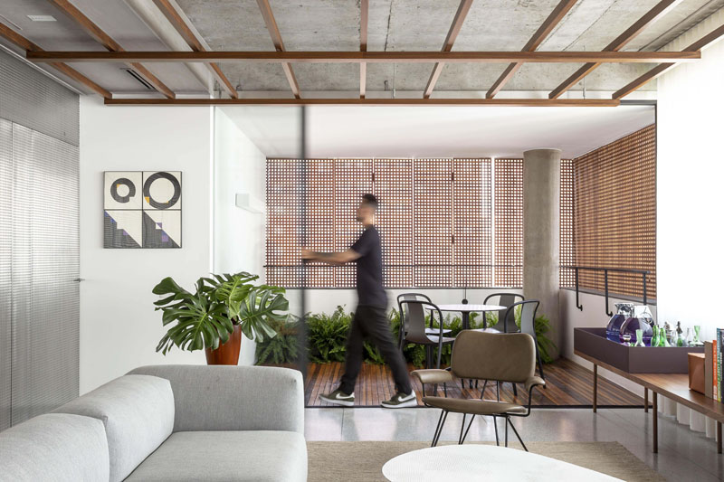 All the flooring in this modern apartment is 'granilite', a polished mix of concrete and small stones, while a sliding glass door connects the living space with a small balcony with a seating area and plants. #ConcreteFloor #ModernApartment #SlidingGlassDoor