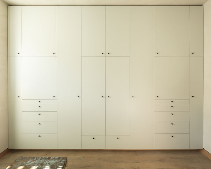 This modern bedroom has a wall of simple, grid-like, built-in cabinets accented with small black gnarled knobs. #Cabinets #CabinetDesign #Storage