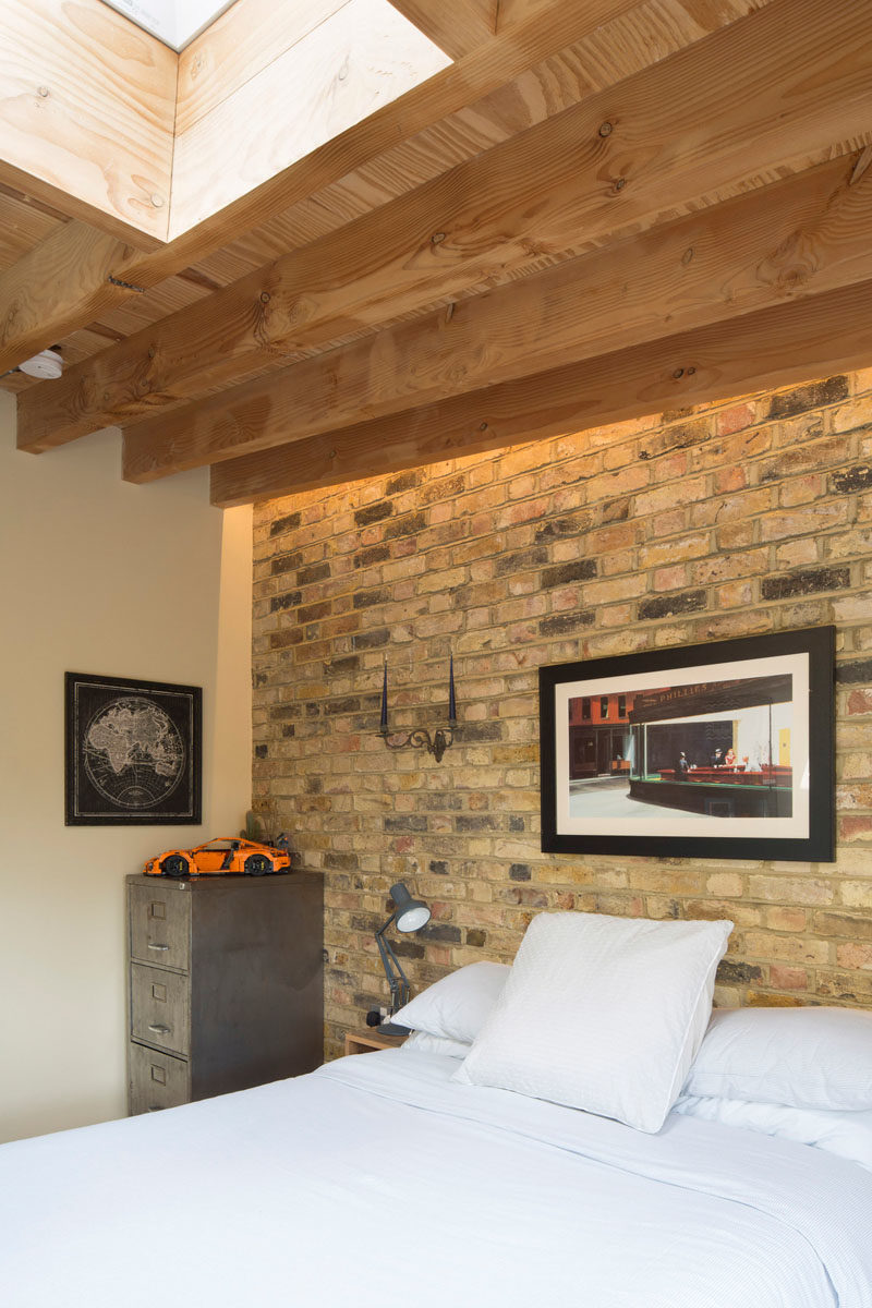 Bedroom Ideas - In this bedroom, a brick wall provides a backdrop for the bed, while wood beams have been left exposed, and a skylight adds natural light. #BedroomIdeas