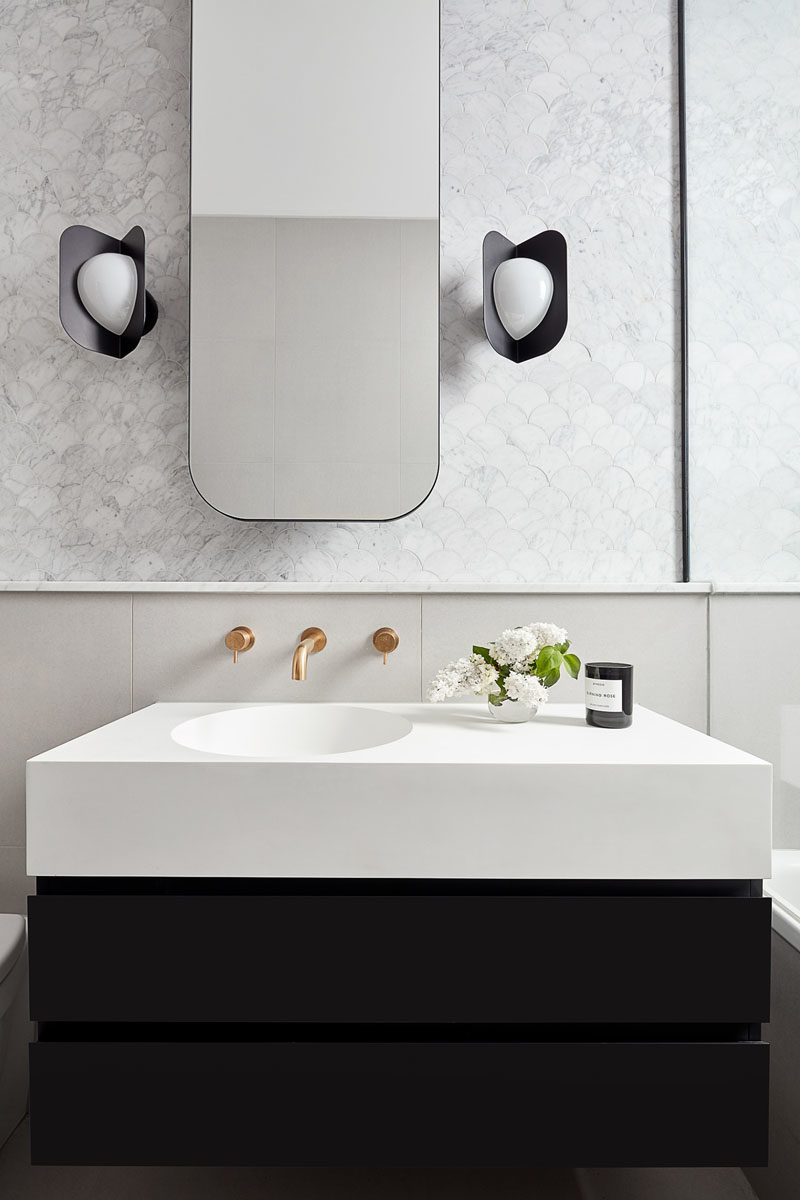 Bathroom Ideas - In this modern bathroom, a rounded rectangular mirror hangs above a small black and white vanity, while the black sconces complement the lower section of the vanity. #BathroomIdeas #ModernBathroom