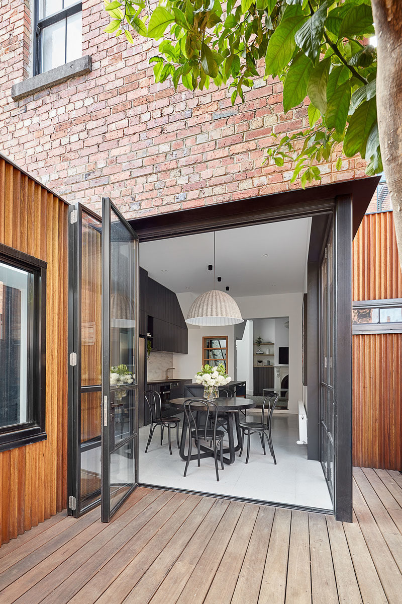 This modern house has folding black-framed glass doors that open the black kitchen and dining area to a small courtyard. #BlackDiningRoom #BlackKitchen #FoldingDoors #GlassDoors