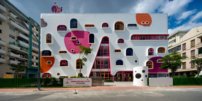 Facade Ideas - The white facade of the kindergarten features pops of color that complement the colorful geometrically shaped window frames. #FacadeIdeas #Architecture #UniqueWindowShapes