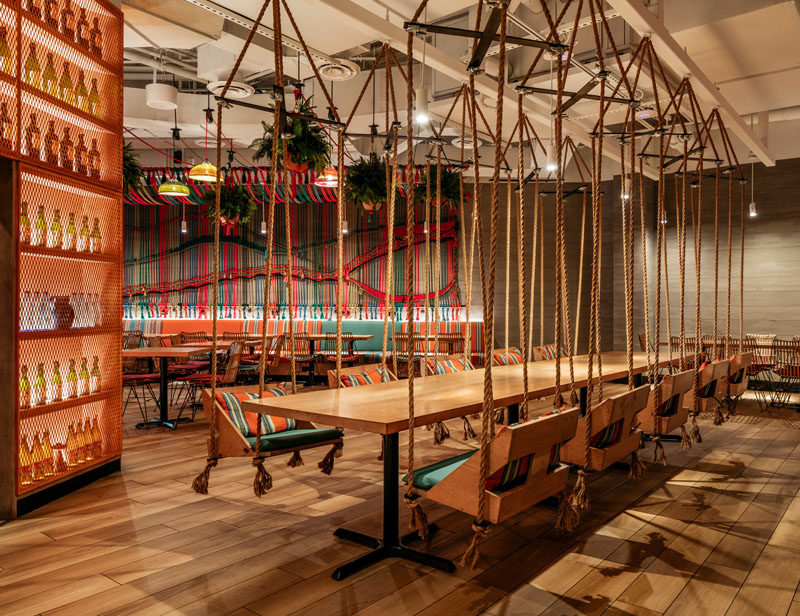 Restaurant Ideas - In this modern restaurant, a large wood communal table is surrounded by swinging chairs, adding to the playful, relaxed vibe of the space. #RestaurantIdeas #RestaurantSeating #HangingChairs