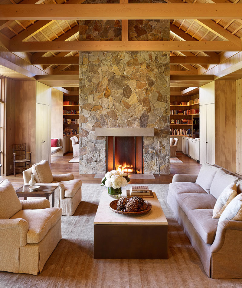 Fireplace Ideas - Exposed timber ceilings in this farmhouse modern interior, lend a sense of rustic refinement that is complemented by the stone fireplace that separates the den and living room. #StoneFireplace #FireplaceIdeas #LivingRoom