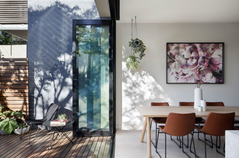 Dining Room Ideas - In this modern dining area, artwork hangs on the wall, while plants hang from the ceiling, and folding glass doors open to the deck and yard. #DiningRoomIdeas #FoldingDoors #DiningRoom