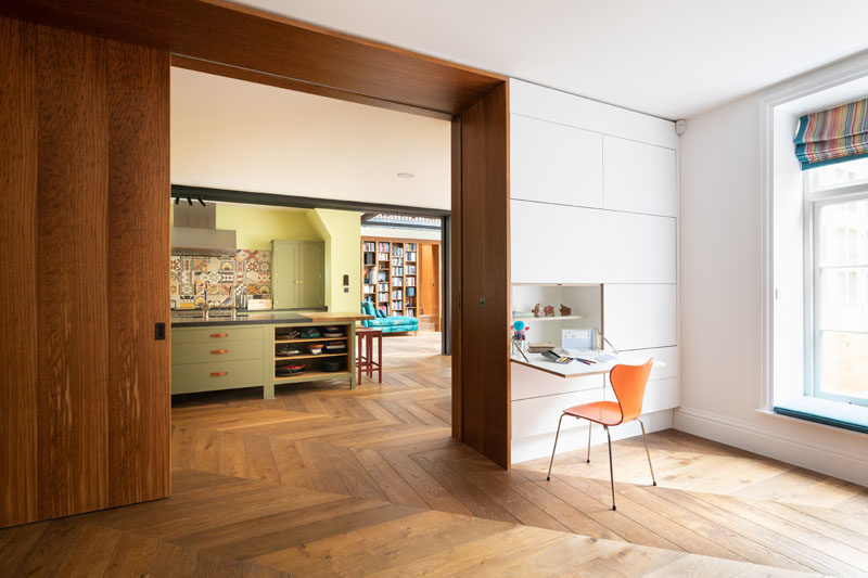 Wall Desk Ideas - This modern playroom has a window seat and  twin hidden writing desks that fold-down from the wall. A large wood pocket door connects the playroom with the kitchen and dining area. #WallDesks #WindowSeat #LargeWoodDoor #PocketDoor