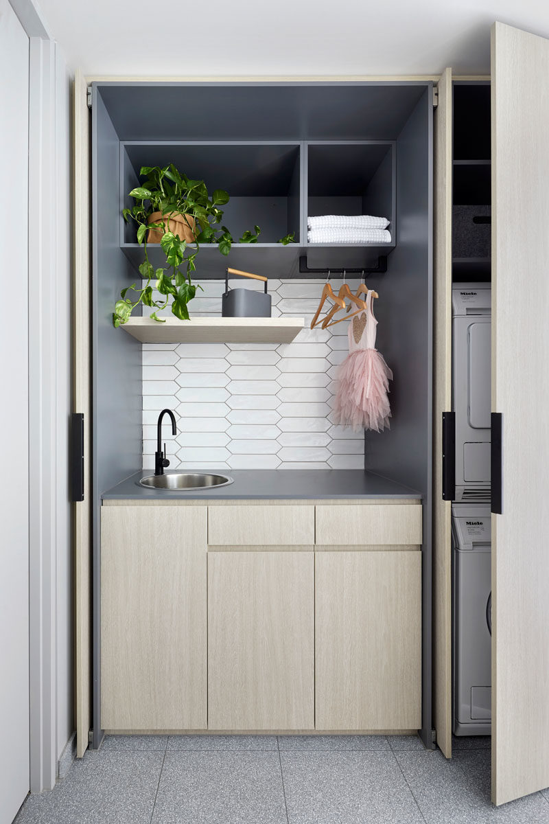 Hidden Laundry Ideas - In this modern white bathroom,  white picket tiles cover the walls, while the laundry is hidden away in wood cabinets opposite the vanity. #BathroomIdeas #PicketTiles #WhiteTiles #HiddenLaundry #Laundry #SmallLaundry