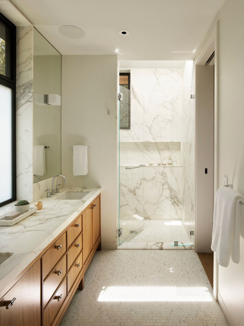 In this modern bathroom, a wood vanity with plenty of storage runs along the wall, while in the shower, a shelf has been built into the wall. #ModernBathroom #BathroomDesign #BathroomIdeas