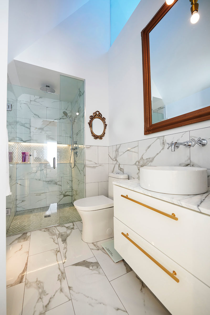 Bathroom Ideas - In this modern master bathroom, a skylight adds natural light to the space, while a walk-in shower has a built-in shelf and is enclosed behind a glass door. #BathroomIdeas #ModernBathroom