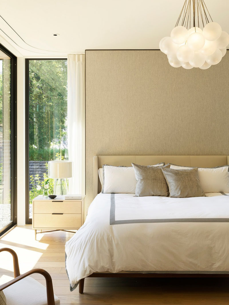 Soft neutral colors have been used in the design of this contemporary bedroom, while floor-to-ceiling windows add an abundance of natural light, and a curtain track has been built-into the ceiling. #BedroomDesign #NeutralBedroom #BedroomDesignIdeas