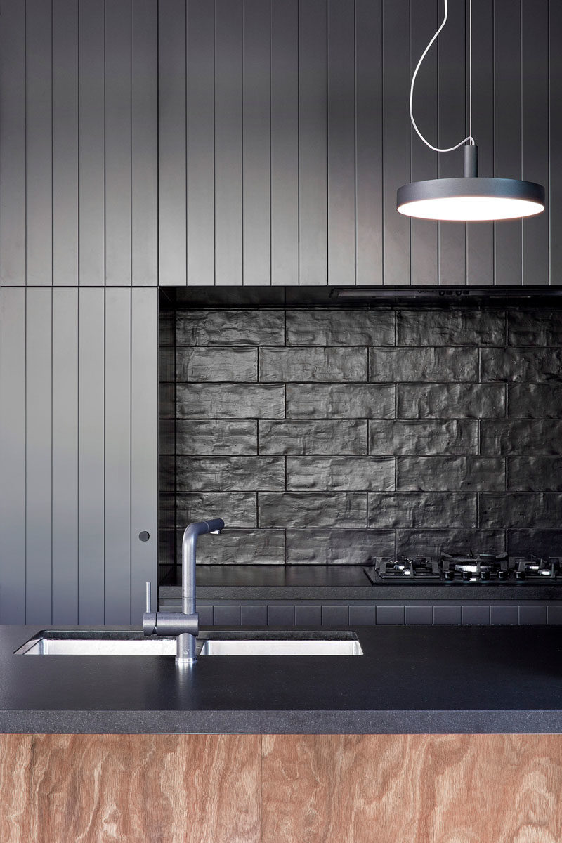 Kitchen Design Idea - Matte black cabinets, black textured tile, and black countertops have been installed in this modern  kitchen, creating a bold and strong appearance. #BlackKitchen #KitchenDesign #DarkKitchen