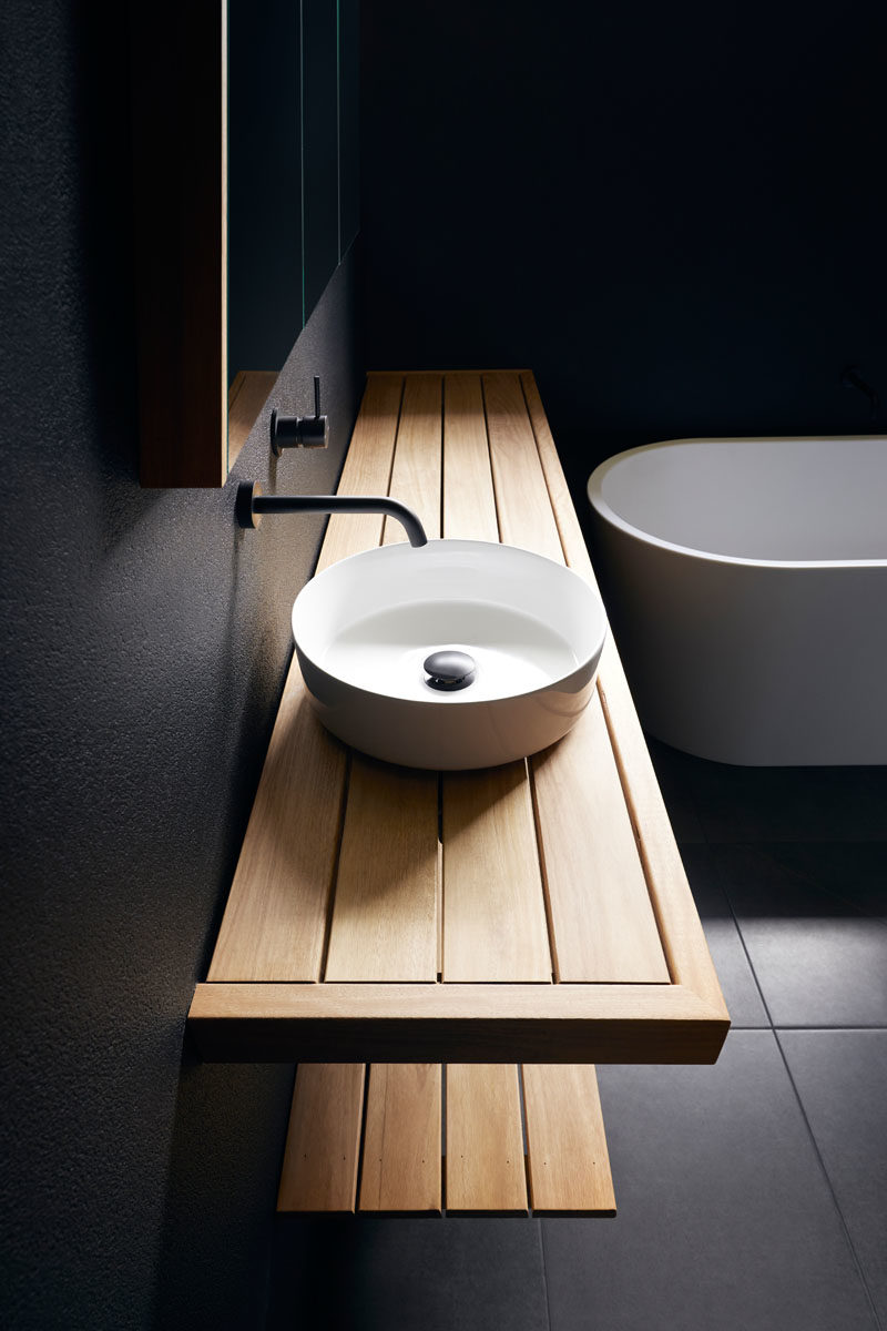 This modern bathroom has matte black walls, a wood vanity, and a white basin and bathtub. #BlackBathroom #ModernBathroom