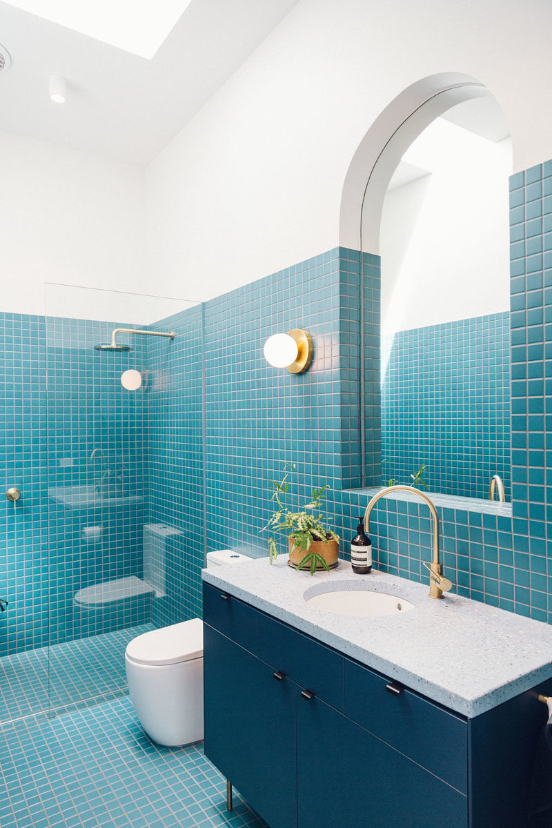 Bathroom Ideas - This modern bathroom features bright blue small square tiles, a skylight, and a curved mirror, fulfilling the home owners' request of an interior that's fun, curvy, colorful, and full of light. #BathroomIdeas #BathroomDesign #BlueBathroom