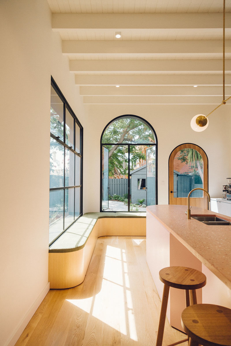 Seating Ideas - A custom designed corner bench, which features a curved wood base and a thin upholstered cushion, creates a place to enjoy the views of the backyard through the black-framed windows. #WindowSeat #WindowBench #BlackFramedWindows #CornerBench