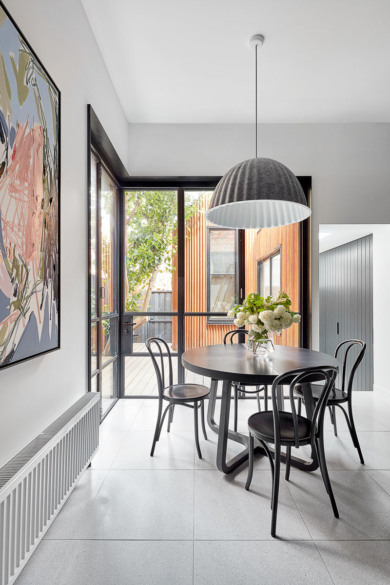 Dining Room Ideas - This modern dining area has been furnished with a round black table that's anchored in the open space by a large grey and white pendant light. #DiningRoomIdeas #InteriorDesign