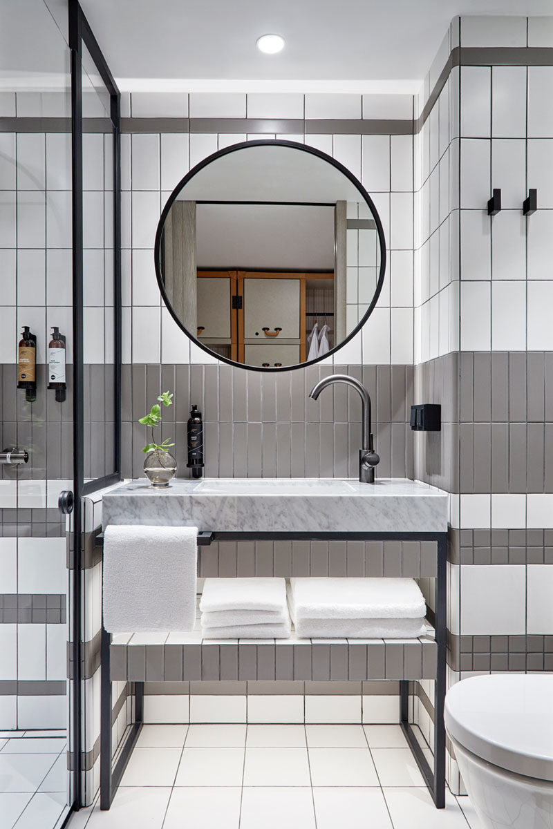 Bathroom Ideas - In this modern bathroom, grey and white tiles have been accented by black elements, like in the vanity, shower frame, mirror, and wall hooks. #ModernBathroom #BathroomIdeas #BlackBathroomAccents