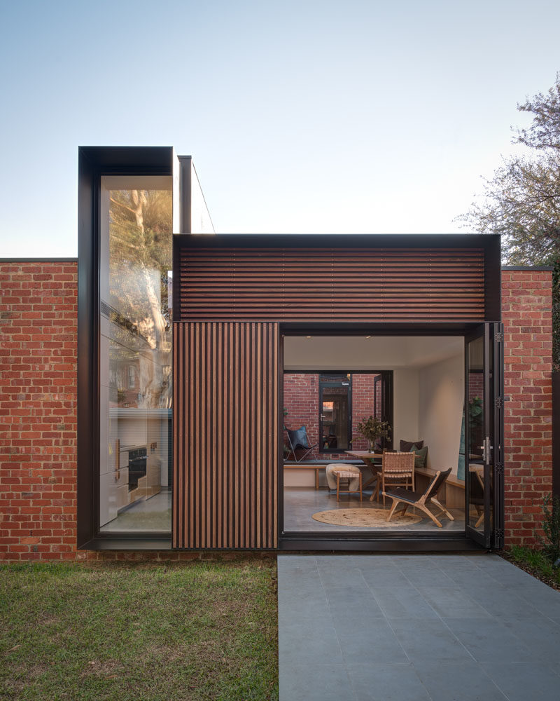 The view from the yard of this modern house addition, showcases the new brickwork that used recycled bricks to tie in with the original house, wood accents, and the deep steel frames. #HouseAddition #Architecture #ModernHouse